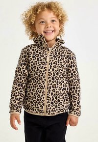 Giacca con zip a stampa leopardata in tonalità marrone chiaro e nera, realizzata in tessuto morbido, con collo alto e tasche laterali. Bambino che indossa pantaloni neri.