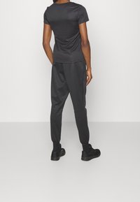 Svart atletisk tröja och matchande joggers, tillverkade av slätt tyg. Joggersarna har elastiska muddar och sidofickor, designade för komfort.