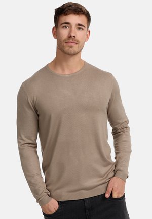 Maglione a maniche lunghe con collo rotondo in beige chiaro, caratterizzato da un motivo a maglia strutturata e polsini a coste, abbinato a jeans scuri.