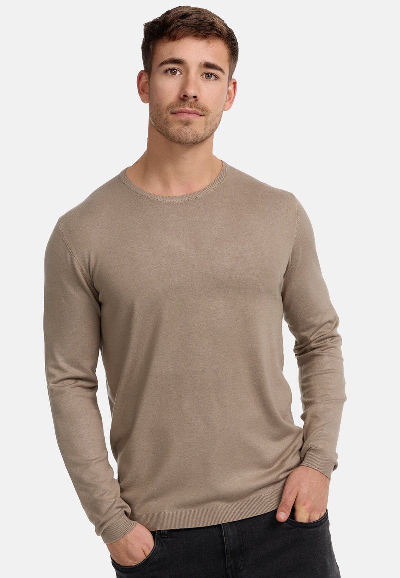 Maglione a maniche lunghe con collo rotondo in beige chiaro, caratterizzato da un motivo a maglia strutturata e polsini a coste, abbinato a jeans scuri.