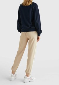 Granatowy sweatshirt z bufkami, beżowe joggery zwężane z elastycznymi mankietami oraz białe sneakersy z delikatnymi akcentami kolorystycznymi.
