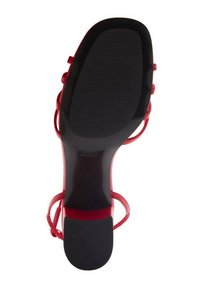 Sandal cu toc roșu, cu fâșii subțiri. Design cu vârful deschis, talpă texturată neagră și o siluetă elegantă. Material roșu neted și accesorii minime.