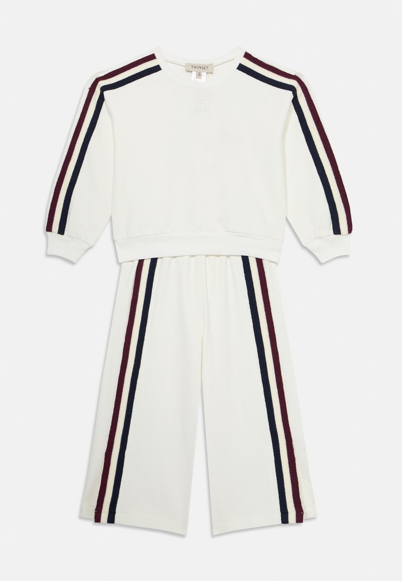 Biały dwuczęściowy zestaw z bluzą z długim rękawem oraz dopasowanymi spodniami z szerokimi nogawkami, oba akcentowane pionowymi paskami w kolorze bordowym i granatowym.