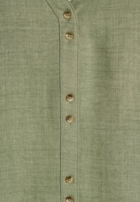 La camicia button-up in lino verde presenta un colletto classico e sei bottoni rotondi lungo la parte frontale, evidenziando una sottile texture e una finitura tessuta.