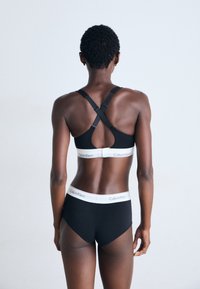 Zwarte sportbeha met verstelbare kruisbanden en een brede elastische band. Zwarte naadloze slip met een witte merkband.