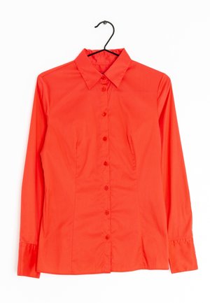 Leuchtend rotes langärmliges Hemd mit Knöpfen und Kragen, aufgehängt an einem schwarzen Bügel vor weißem Hintergrund.