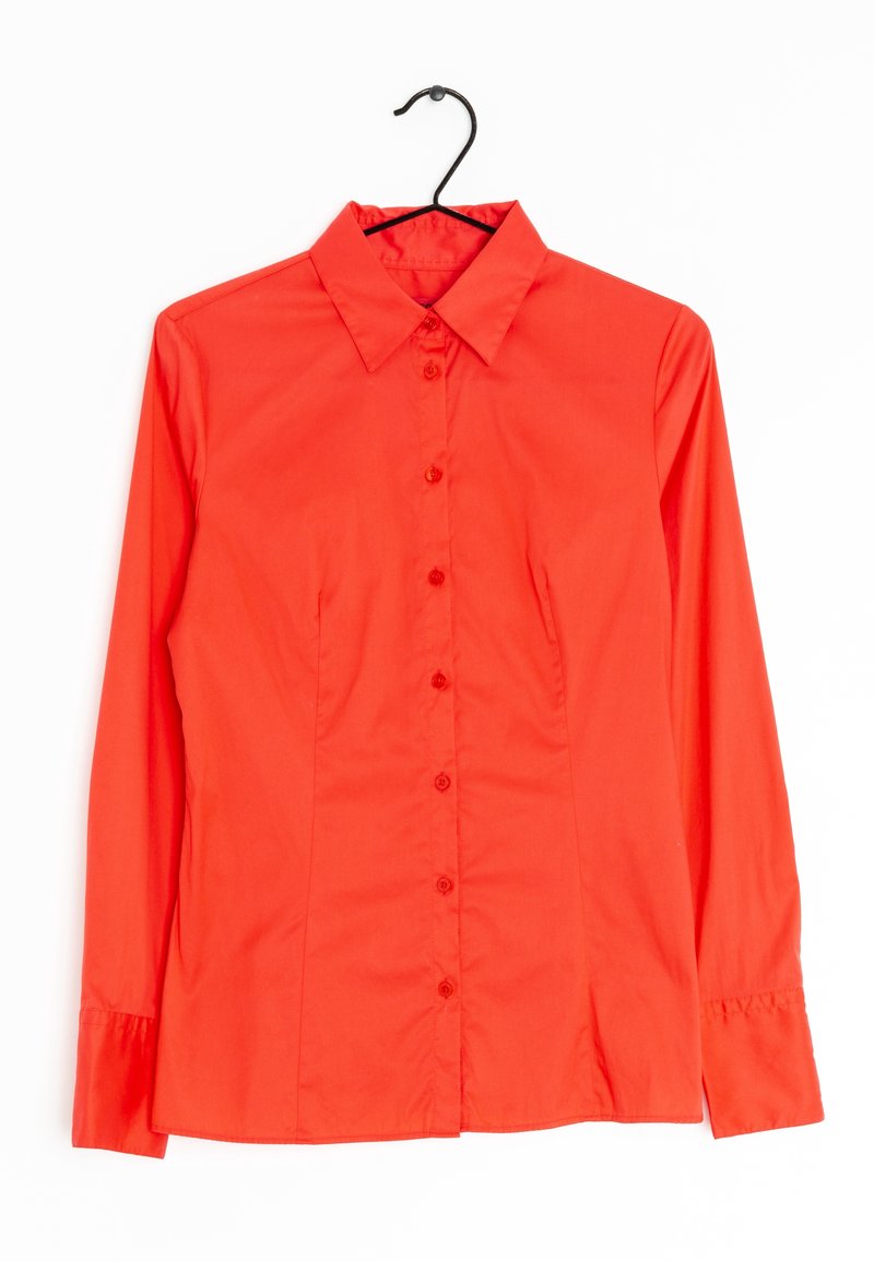 Chemise rouge vif à manches longues avec boutons et col, suspendue sur un cintre noir contre un fond blanc.