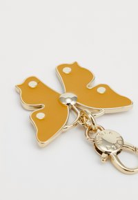 Yellow butterfly-shaped keychain with gold accents, glossy finish, and three circular white embellishments. Includes a metallic clasp attachment.