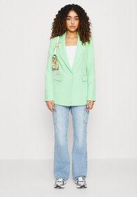 Mintgrønn blazer med hakkeslag og klaffc lommer, kombinert med lyseblå vide jeans og en liten mønstret håndveske. Søte sølvfargede sneakers fullfører antrekket.