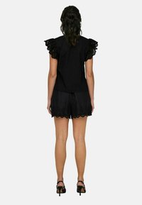 Haut noir avec des détails en dentelle aux manches, associé à un short noir avec des bords festonnés et des découpes florales. Texture lisse, design élégant.