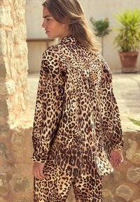 Set van een glanzende leopardprint blouse en broek, met een relaxte pasvorm, lange mouwen en stijlvolle manchetten. Aardetinten domineren.