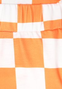 Oranje en wit geruite stof, met een aangesloten elastische taille. De textuur lijkt zacht en katoenachtig, met gedurfde contrasterende patronen.