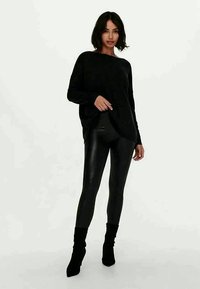 Sort oversized sweater med en blød tekstur, parret med højglansede sorte leggings. Modellen har tætsiddende sorte ankelstøvler på.