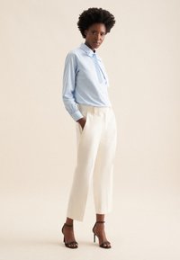 Helles blau gestreiftes Hemd mit Knöpfen, weiße hochtaillierte Hosen und schwarze Riemchensandaletten. Glatte Texturen, taillierte Passform und klassisches Design.