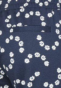 Marinblått tyg med ett spritt blommönster i vitt och ljusblått, med en infälld ficka och gather vid midjan.