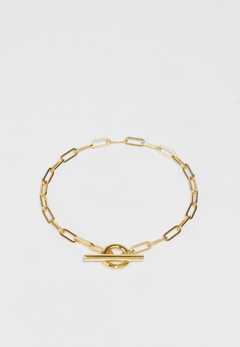 Kuldne käevõru, millel on piklikud ovaalsed lingid, ümmargune lukustusklamber ja T-kujuline accent sulgemiseks. Sile metalline viimistlus.