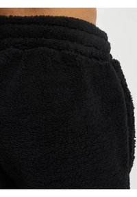 Svart fleece joggebukser med en teksturert overflate, som har elastisk midje og rynkede mansjetter for en tettsittende passform.