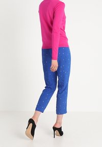 Tiukka vaaleanpunainen neulepusero ja siniset lyhytlahkeiset housut, joissa on kultaisia täpliä. Mustat korkokengät. Sileä pinta ja kirkkaat värit.