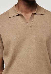 Polo à manches courtes en tissu tricot léger marron clair, présentant un col classique, un design en V et une texture lisse et douce.