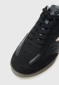 Fekete sportcipő nubuk bőr felsőrésszel, bőr díszítésekkel, kerek fűzőkkel, párnázott szegéllyel és áttetsző gumi talppal.