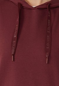 Bordový hoodie s kapucí a šňůrkami, na kterém je nápis "S. OLIVER". Měkký bavlněný materiál a uvolněný střih s klokankovou kapsou.