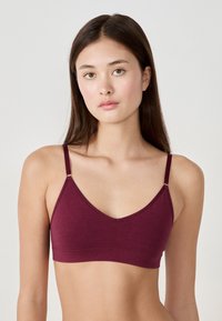 Bordowy biustonosz braletka wykonany z miękkiego materiału, z cienkimi regulowanymi ramiączkami i dekoltem w serek. Gładka faktura z minimalnymi detalami.