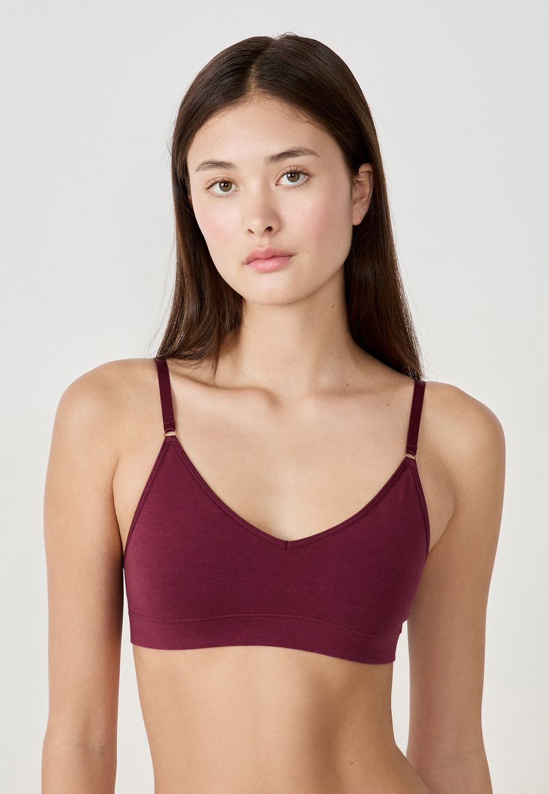 Bordowy biustonosz braletka wykonany z miękkiego materiału, z cienkimi regulowanymi ramiączkami i dekoltem w serek. Gładka faktura z minimalnymi detalami.