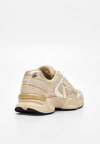 Béžová a zlatá sportovní obuv s robustní podrážkou, síťovaným a koženým svrškem a značkou "Replay" na patě, zobrazena zezadu v úhlu.