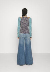 Långärmad topp med ett blandat blått och lila mönster på en åtsittande kropp, ihopparad med vida, högmidjade denimjeans med rå kant.