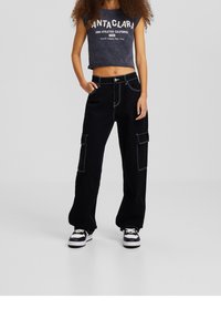 Svarta cargo byxor med vit sömnad, som har två sidfickor och en avslappnad passform. Matchas med en mörk, kort grafisk tanktop.