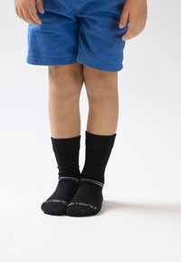 Sorte crewsokker med ribbede manchetter og hvide striber, båret med blå shorts, der viser en tætsiddende pasform og blød tekstur.