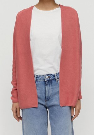 Osoba ubrana w luźny, otwarty różowy sweter z dzianiny noszony na biały t-shirt z okrągłym dekoltem oraz jasnoniebieskie, wysokie spodnie dżinsowe.