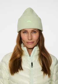 Vaaleanvihreä ribattua beanie-hattu, jossa on kärjellinen yläosa ja pieni logopatchi, yhdistettynä kiiltävään, vaaleanvihreään vetoketjulliseen takkiin.