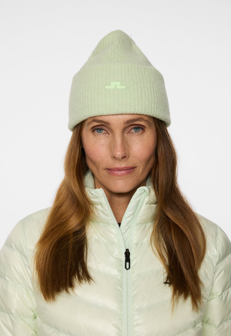 Vaaleanvihreä ribattua beanie-hattu, jossa on kärjellinen yläosa ja pieni logopatchi, yhdistettynä kiiltävään, vaaleanvihreään vetoketjulliseen takkiin.