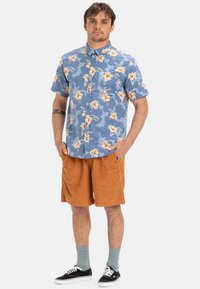 Korte mouwen blauwe shirt met bloempatroon, tan corduroy shorts, grijze sokken en zwarte sneakers. Casual pasvorm met een button-down kraag.