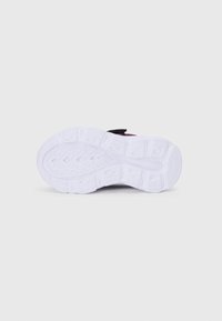 Semelle en caoutchouc blanc avec des rainures profondes et des motifs de semelle, faisant partie d'une chaussure de sport noire et rose vue par le dessous sur un fond uni.