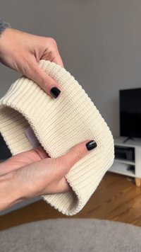 Pletený čelenka v krémové barvě, s vroubkovanou texturou a skládacím designem, s jemným štítkem na okraji.