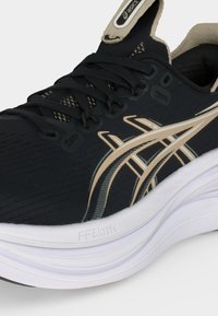 Μαύρο και μπεζ παπούτσι τρεξίματος Asics με μαύρα κορδόνια, μπεζ λογότυπο, μαξιλαρωτή λευκή σόλα και επενδεδυμένο κολάρο αστραγάλου.