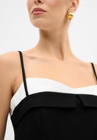 Czarna i biała sukienka z cienkimi ramiączkami, dekoltem w kształcie serca i akcentem w postaci kokardy na koronkowym bodice, o gładkiej fakturze materiału.