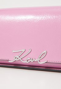 Rosa Leder-Wallet mit glänzender Oberfläche, silbernem metallischem Signaturlogo und kontrastierendem schwarzen Stich entlang der Kante.
