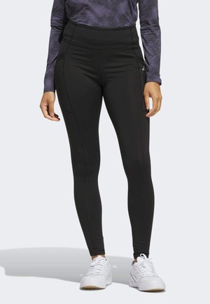 Leggings neri a vita alta realizzati con un tessuto morbido e stretch, con cuciture laterali e una fascia in vita piatta, abbinati a scarpe da ginnastica bianche.