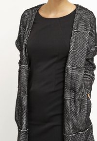 Black, fitted dress with short sleeves and a scoop neckline, layered with a black and white textured cardigan featuring an open front.