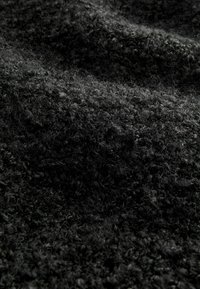 Black textured fabric with a fuzzy surface, featuring a dense, soft weave and subtle variations in shade. Looks plush and warm.