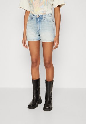Shorts di denim celeste con orlo sfrangiato, abbinati a stivali neri in pelle al ginocchio con tacco basso a blocco e zip laterali.