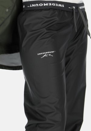 Schwarze wasserdichte Hose aus glattem, glänzendem Material mit elastischem Bund. Mit dem Logo "SWEDEMOUNT" und einer Berggrafik in Weiß.