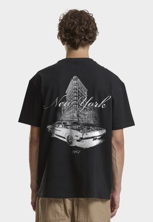 Hombre con camiseta negra con un gráfico blanco de un edificio de Nueva York, un coche clásico y el texto "Nueva York 1964" en la espalda.