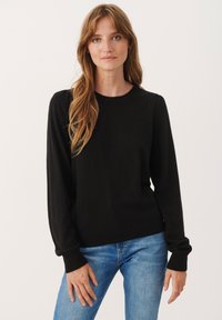 Sort, langærmet sweater med rund hals og ribbede manchetter, der har en tætsiddende stil og blød strikket tekstur. Bæres med blå jeans.