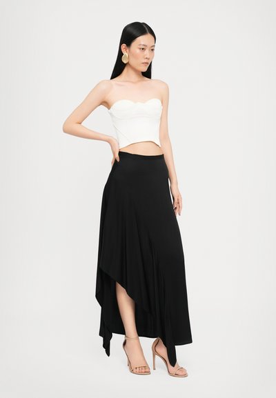 Biely top bez ramienok s textúrovanými detailmi skombinovaný s dlhou, asymetrickou čiernou sukňou. Modelka má na sebe nahé sandále na remienky.