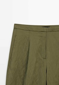 Pantalon taille haute vert olive avec plis devant et poches latérales, fabriqué en tissu léger.