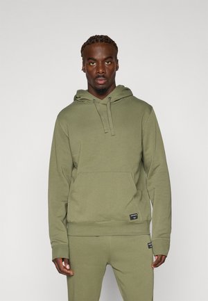 Oliven grønn hettegenser laget av myk stoff, med en frontlomme, justerbar snorhette og ribbede mansjetter. Minimal merking på kanten.
